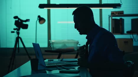 medium silhouette video of a detective policeman sitting in the interrogation room smoking working medium silhouette video of a detective policeman sitting in the interrogation room smoking working on a laptop and studying a knife from the evidence true crime documentary creative content