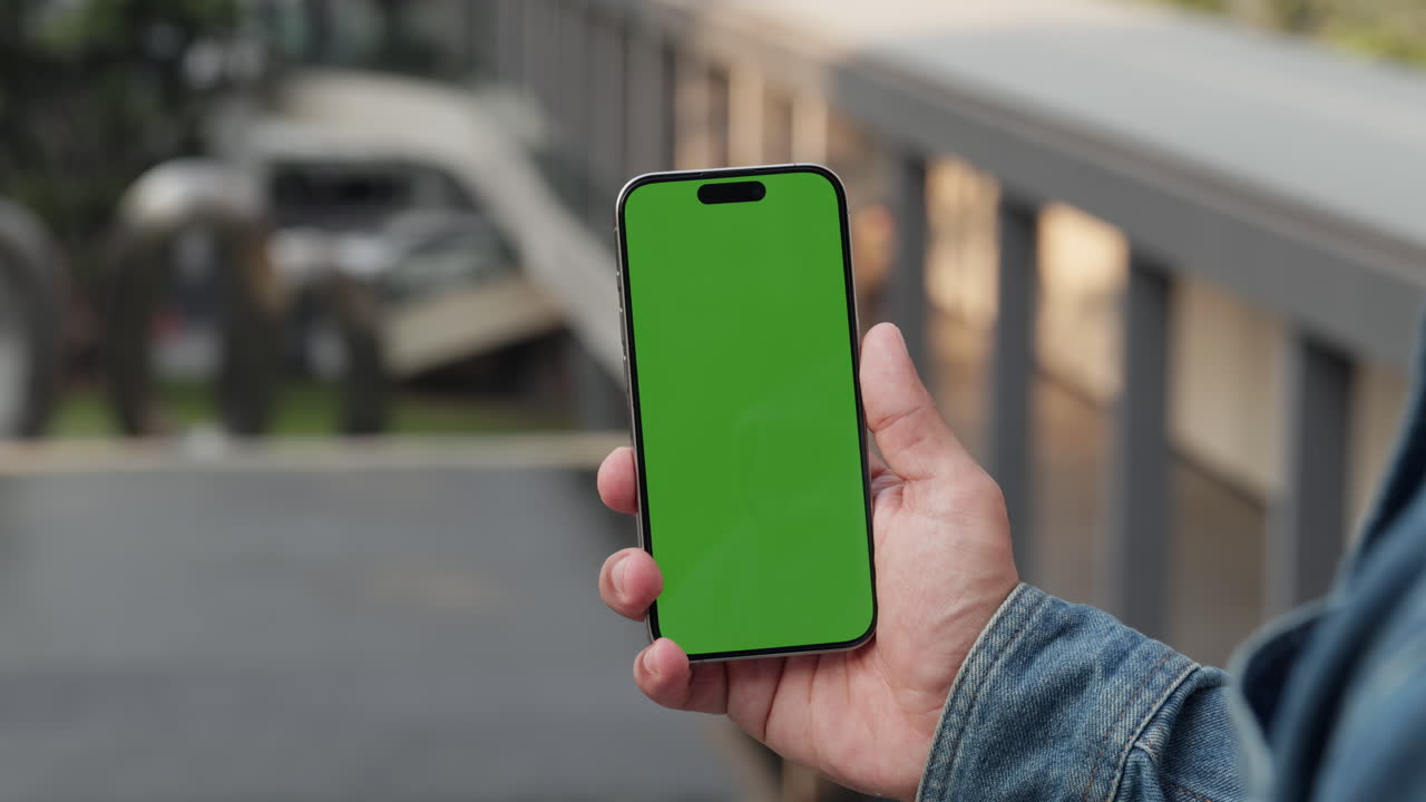 Persona che tiene in mano uno smartphone con schermo verde all'aperto