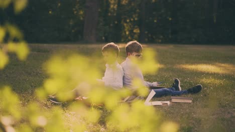 школьники читают книги, делая домашние задания на пышной траве в парке.