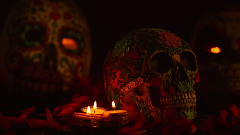 close up on still life of decorated skulls surrounded by candles and flower petals celebrating mexican holiday of dia de muertos or day of the dead