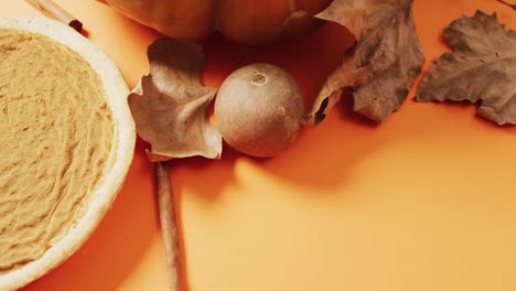 Video-of-autumn-leaves,-pumpkin,-spices-and-pie-on-orange-background