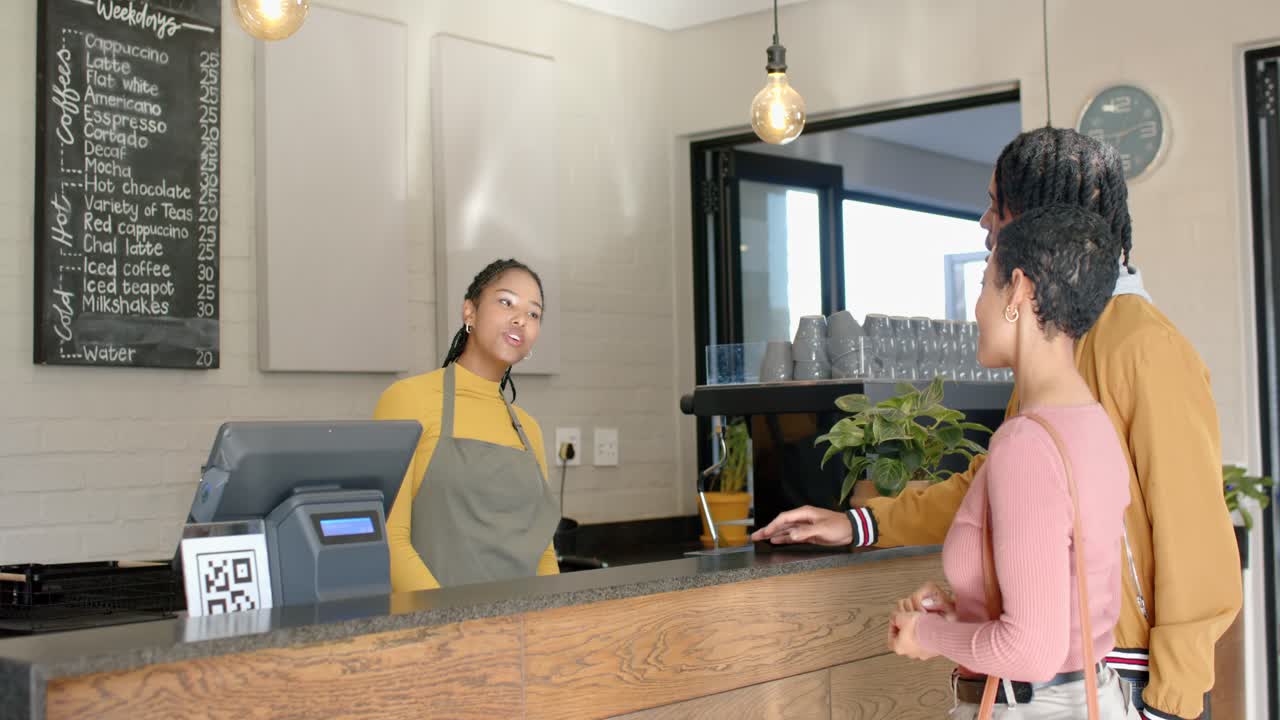 Female barista at cafe counter answering query pointing at menu listing coffee options, copy space