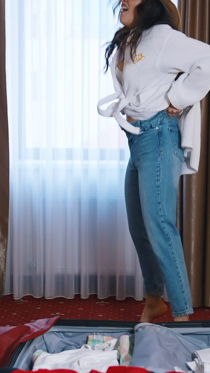 Young woman dressing in the hotel. Smiling girl trying to put on her jeans after the vacation. Woman puts on the weight during holidays. Vertical video
