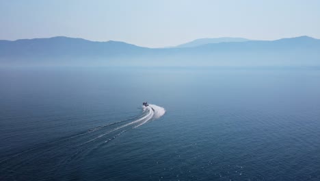 speed boat driving fast in curves over deep, blue okanagan lake on a hot day during canadian wildfire season