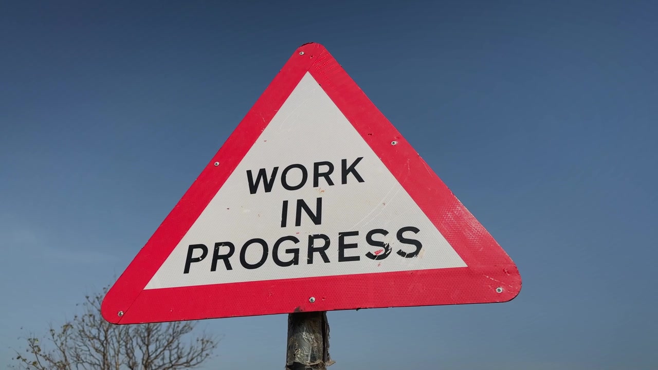 Camera orbiting around a triangular work in progress warning sign against a clear blue sky The road safety marker highlights ongoing construction activity and infrastructure development