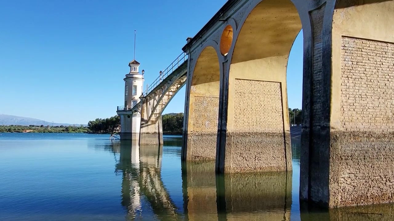 Torre, passerella e ponte di pietra sulle acque del lago in un tramonto colorato. Riflessi nell'acqua di una torre bianca decorata e riflessi d'acqua sul ponte di pietra al tramonto. Granada. Spagna
