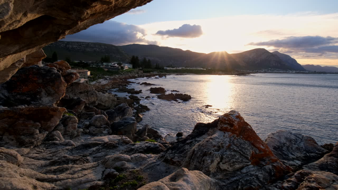 Vivid rays of sunrise over mountain and ocean viewed from rugged Hermanus coast