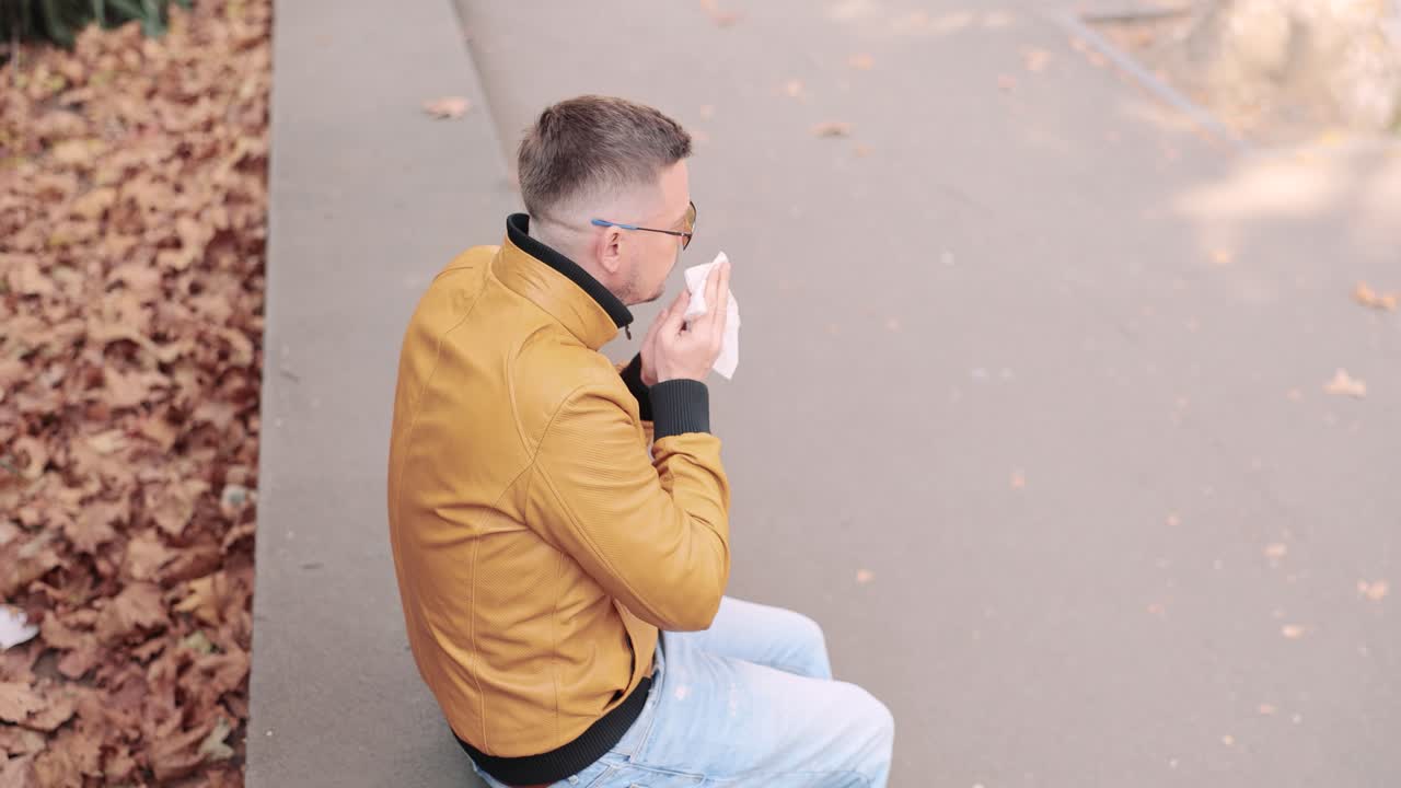 Man with a cold blowing his nose in the park