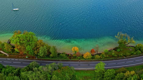 aerial overview of a car on a road on the coast of lake attersee, fall in austria
