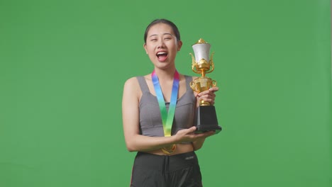 asian woman with a gold medal kissing a gold trophy being proud winning as the first winner on green screen background in the studio