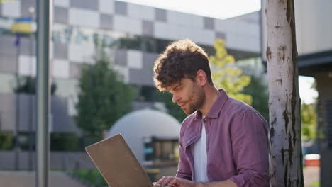 un tipo urbano escribiendo en una computadora portátil a la luz del sol. un trabajador independiente enfocado trabajando al aire libre.