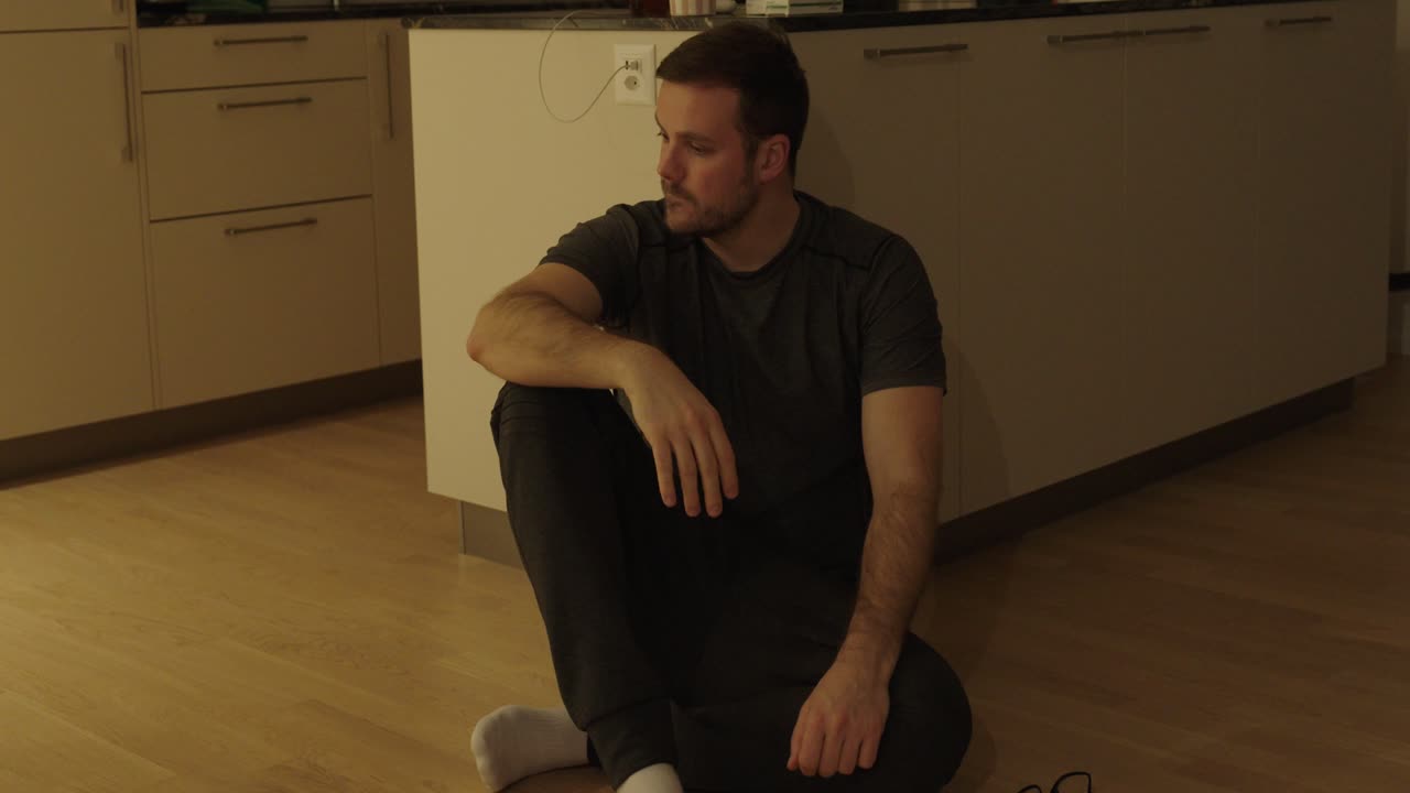 Emotional stock footage showing a man sitting on the kitchen floor in frustration, taking off his glasses in disappointment, then motivating himself to stand up and move on, symbolizing setback, self-