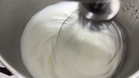 preparation of fluffy and soft swiss meringue buttercream pastry, electric mixer mixing and beating egg white and sugar until it is glossy peak and stiff peak, close up shot