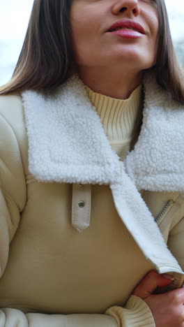 beautiful brunette wrapping herself up in a jacket sitting outdoors. lady spending free time in the autumn park. close up. vertical video