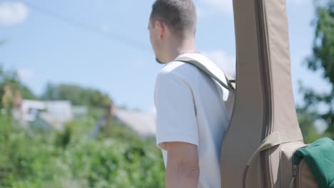 young man walking with guitar on street near forest