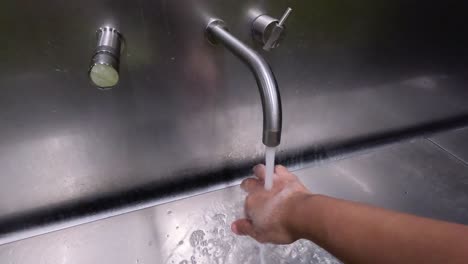 person washing hands in a stainless steel sink