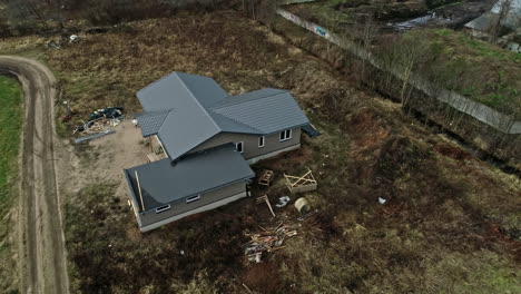 new house with gray roof and dirt driveway road in muddy field, drone