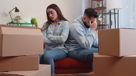 upset family sitting on sofa near cardboard boxes with stuff, long relocation, bankruptcy, bank debt