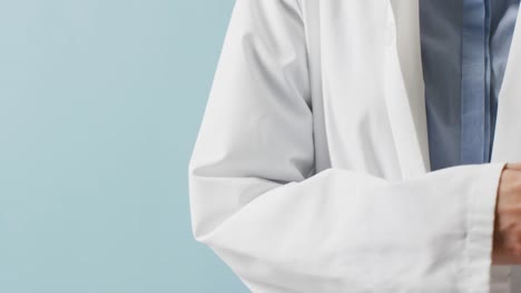 midsection of caucasian doctor holding stethoscope crossing arms, on blue background with copy space