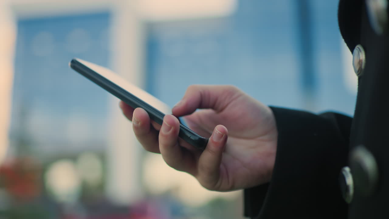 un teléfono inteligente operativo de mano en un entorno urbano moderno con un fondo borroso con edificios de vidrio contemporáneos y vegetación