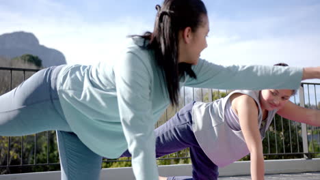 Happy-biracial-mother-and-daughter-practising-yoga-on-terrace-in-sunny-day,-slow-motion