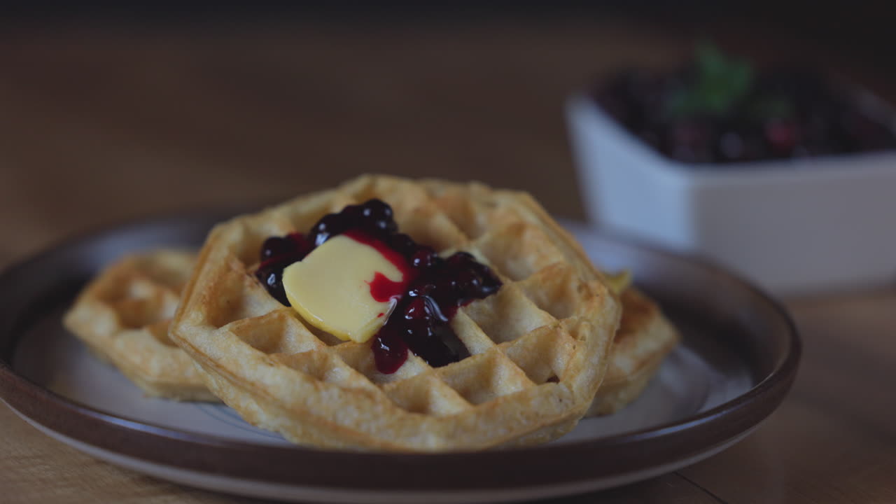 Close-up of golden waffles served with fresh huckleberries, berry jam, and a pat of butter on a rustic plate
