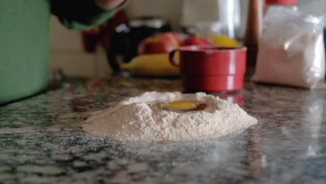 woman cracking an egg on countertop and pouring it over flour ring