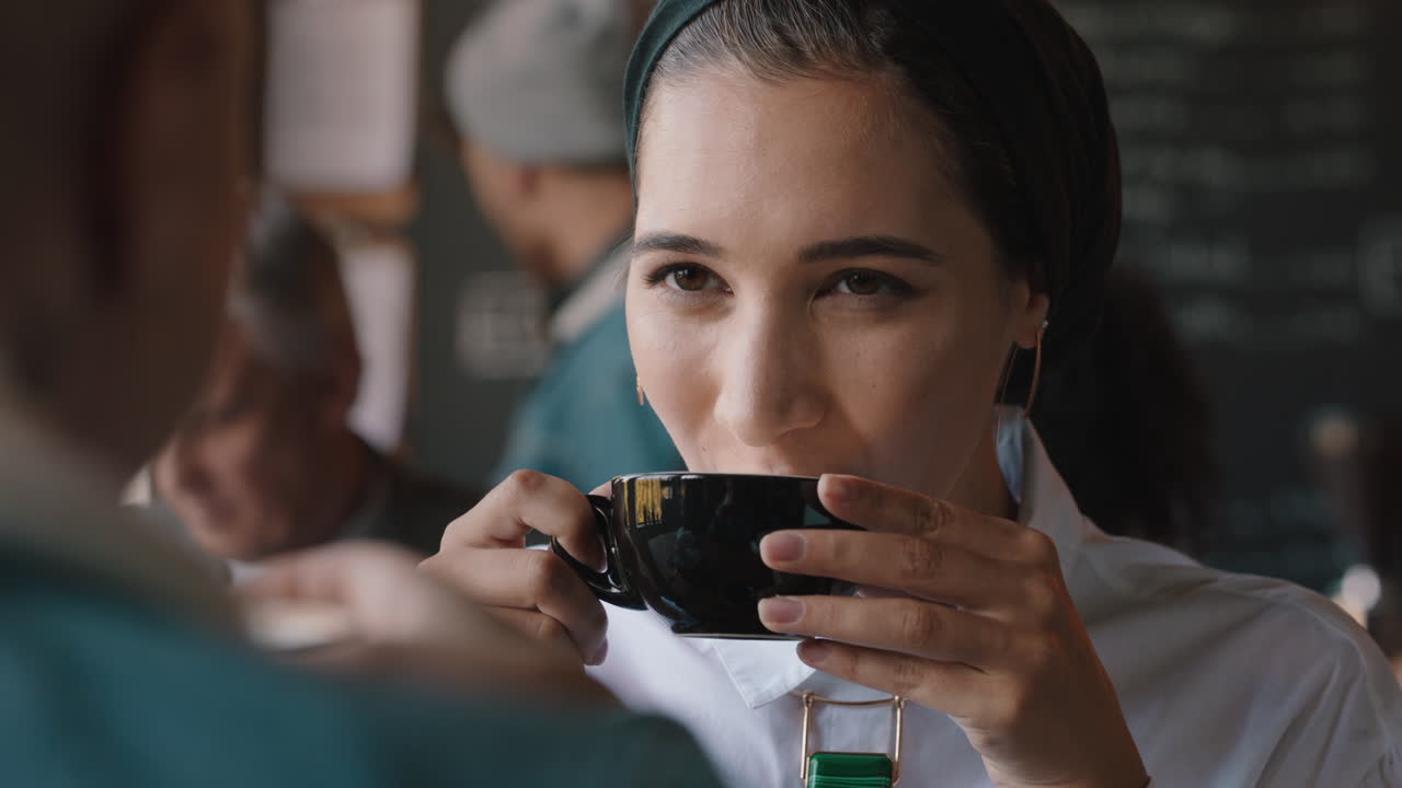 아름다운 무슬림 여성이 카페에서 친구와 채팅하고 커피를 마시고 사교를 즐기고 바쁜 레스토랑에서 대화를 나누고 있습니다.