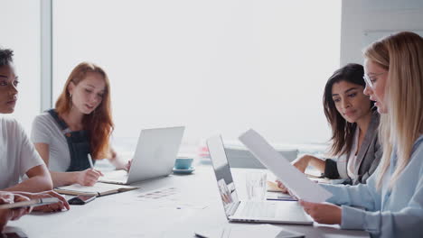 team of young businesswomen meeting around table discussing document or plan in modern workspace