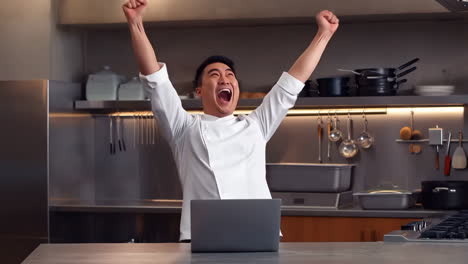 chef achieves success and celebrates in a professional kitchen with his laptop