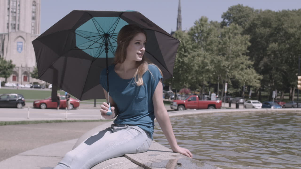 Young Woman Sitting by a Fountain on a Sunny Day