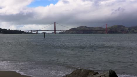 storm clouds roll over the golden gate bridge as waves crash onto the beach in san francisco