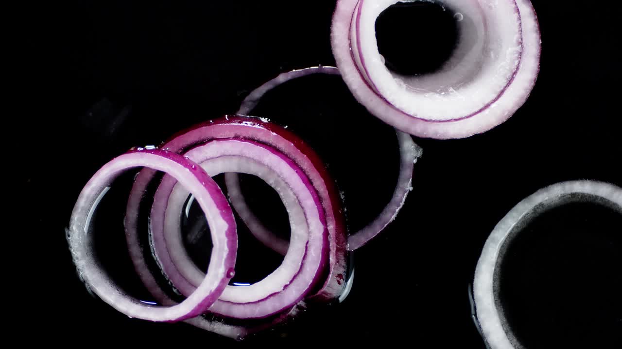 Rings of red onions fall on the water with splashes.