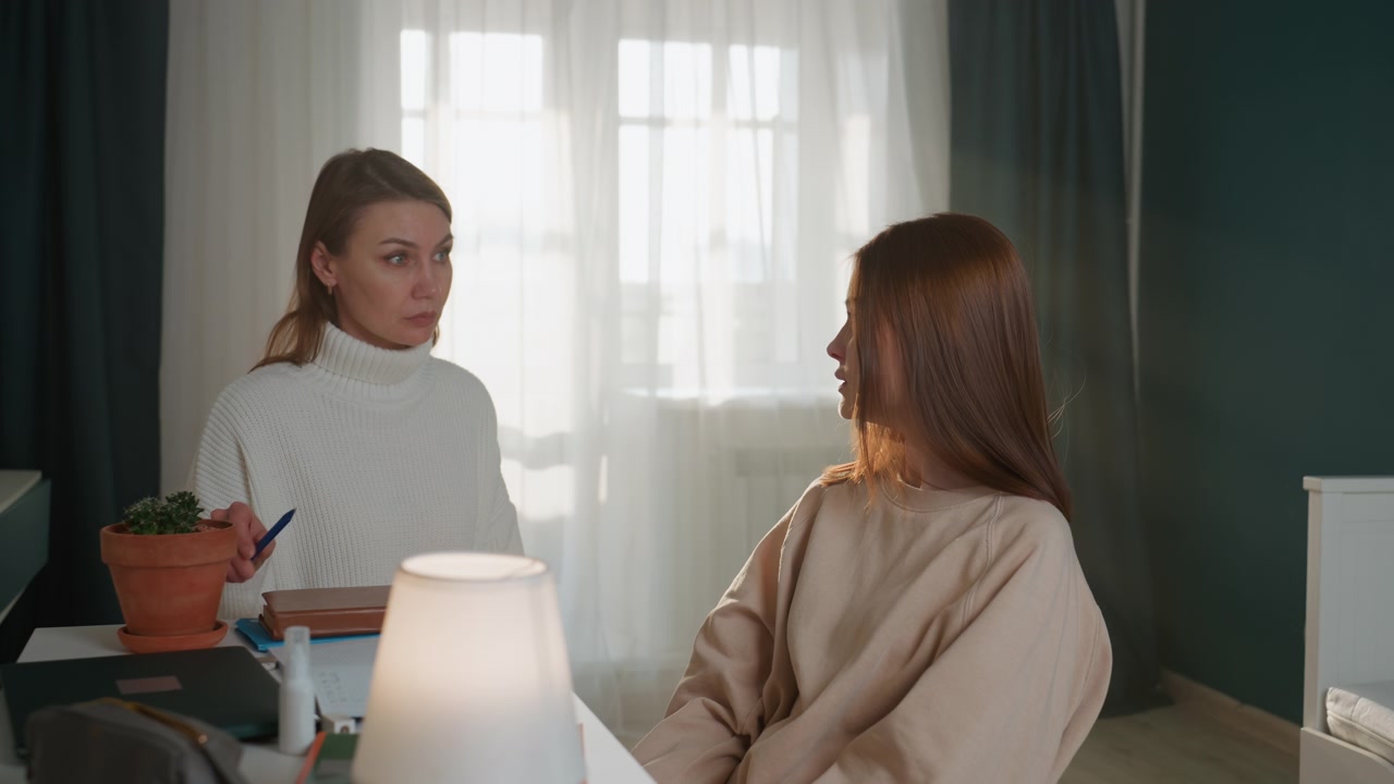 Hvid vejleder coacher en teenagestuderende ved et skrivebord i et hyggeligt hjemmekontor med lampe og potteplante, hvor varmt naturligt lys strømmer ind gennem gardinerne. Vejlederen fungerer som grammatikcoach og mentor, peger på notesbogen og forklarer
