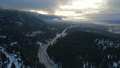 panoramic view of cariboo highway 95 running into the horizon surrounded by impressive mountains range covered in clouds during sunrise warm light: warm light , spectacular aerial approach shot