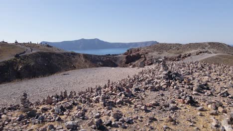 Low-flying-by-stacked-rocks-and-over-volcano-crater-at-Santorini-island,-Greece-in-slow-motion