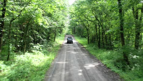 offroad jeep car driving through dense forest road in aerial drone view