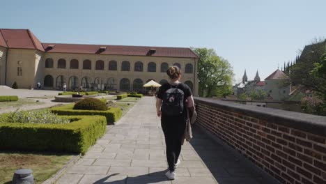 adult woman walking towards the riding school building seeing tower of prague castle at background in czech republic