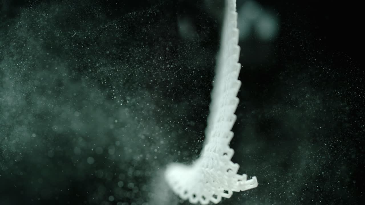 una pequeña pieza de tela blanca derrama polvo en el aire mientras se balancea.