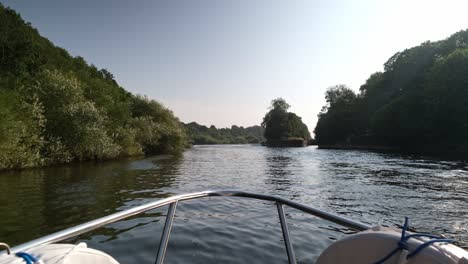 footage from the front of a riverboat and it sails along the river trent with the green surroundings on a bright, clear, sunny, summers day