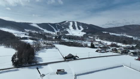 push in drone shot flying above snow covered fields, with ski area and mountain town in distance