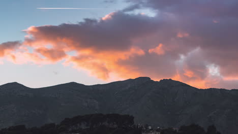 lapso de tiempo de enormes nubes moviéndose rápido sobre y detrás de una montaña durante la puesta de sol