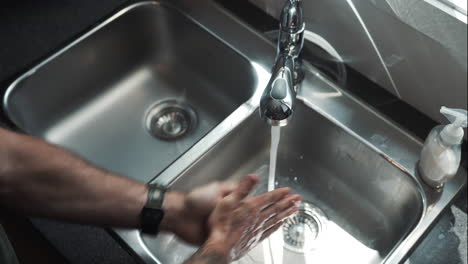 hands wearing watch turn on tap of stainless steel basin and wash hands surgically with soap according to covid-19 - coronavirus guidelines, close up shot