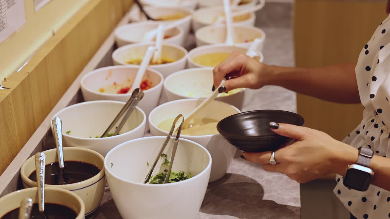 Woman selects and mixes sauces at a well-lit, modern hotpot condiment self-service station