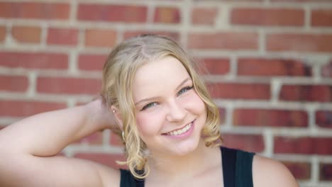 girl lets her hair down outside against a brick wall