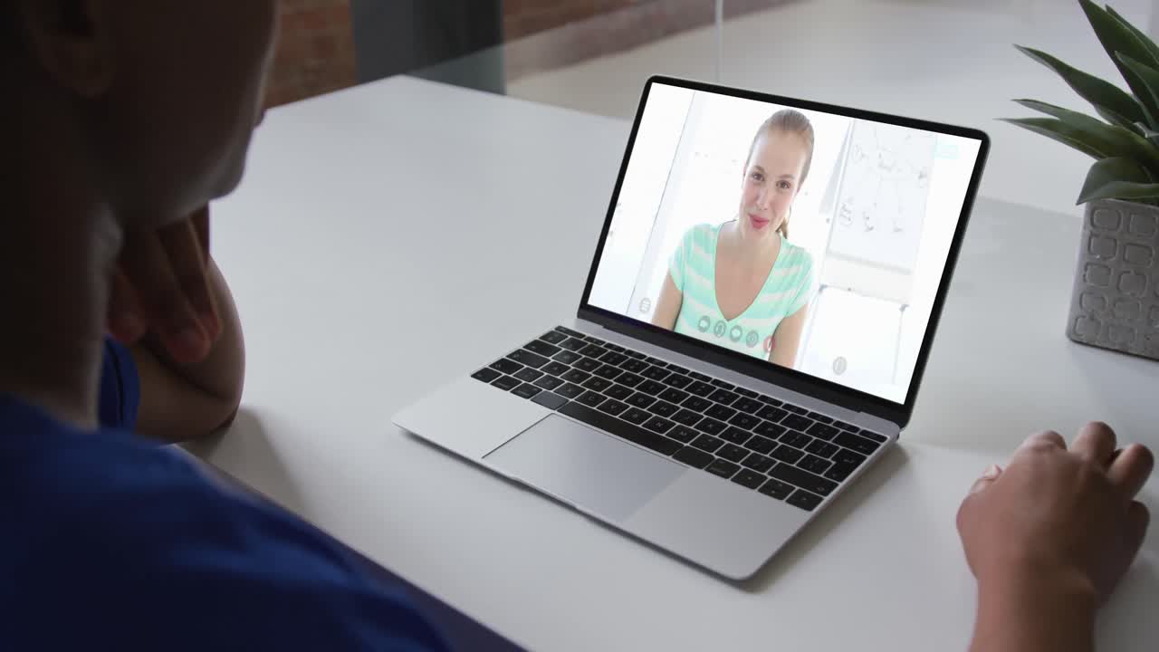 Plano medio de una mujer afroamericana teniendo una videollamada en el portátil con una colega en la oficina.