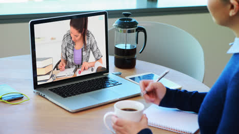 Profesora-Caucásica-Usando-Una-Computadora-Portátil-En-Una-Videollamada-Con-Una-Estudiante,-Tomando-Notas