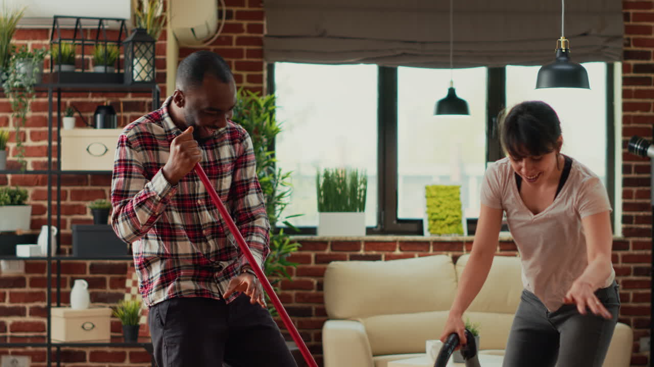 Mixed race smiling couple dancing and cleaning apartment