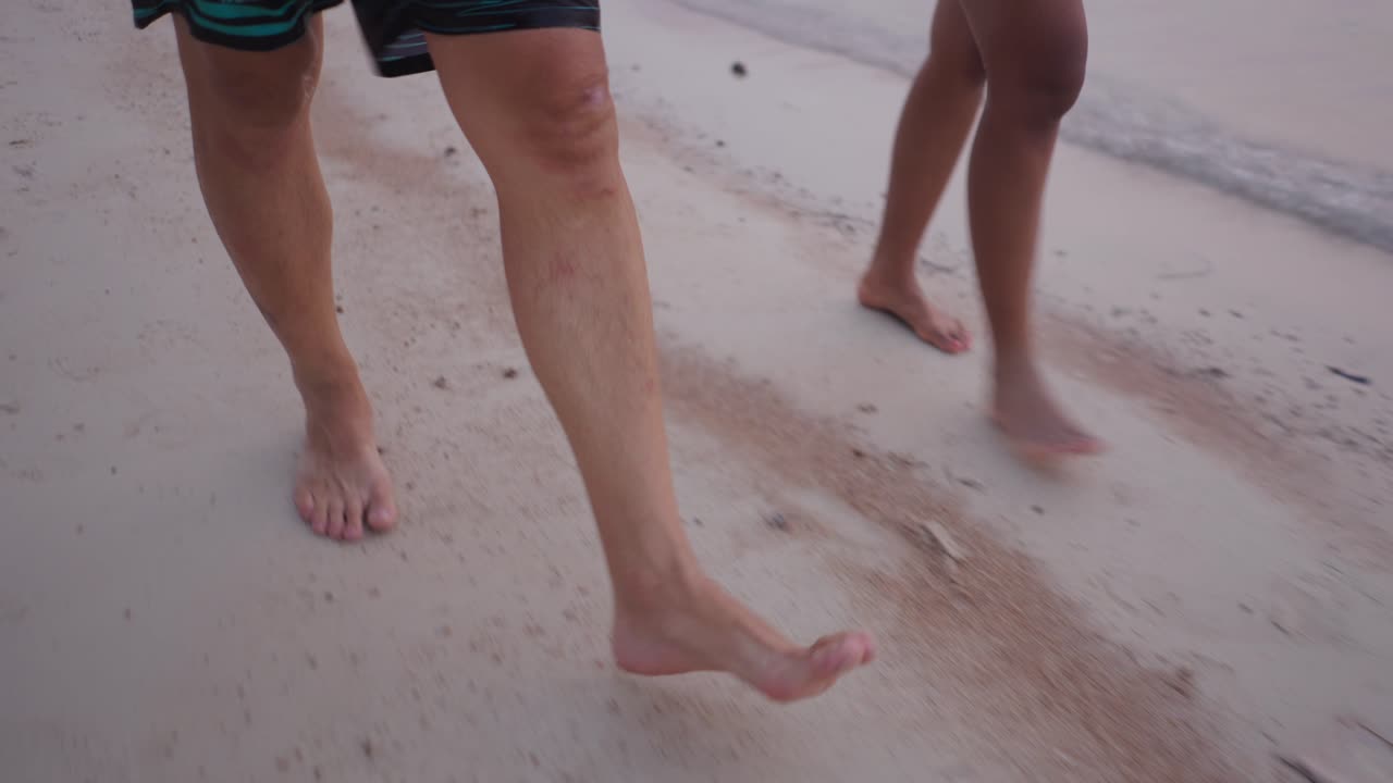 Two people walking barefoot along a sandy beach shore