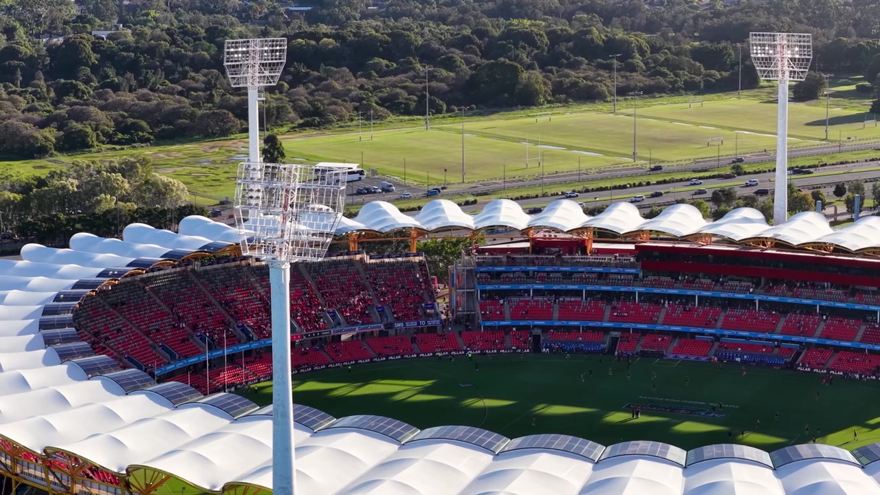 High angle drone shot of a large sports arena with red seating and green turf.